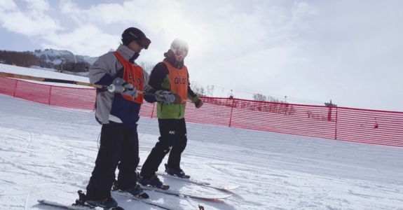 A visually impaired skier skiing with an instructor.