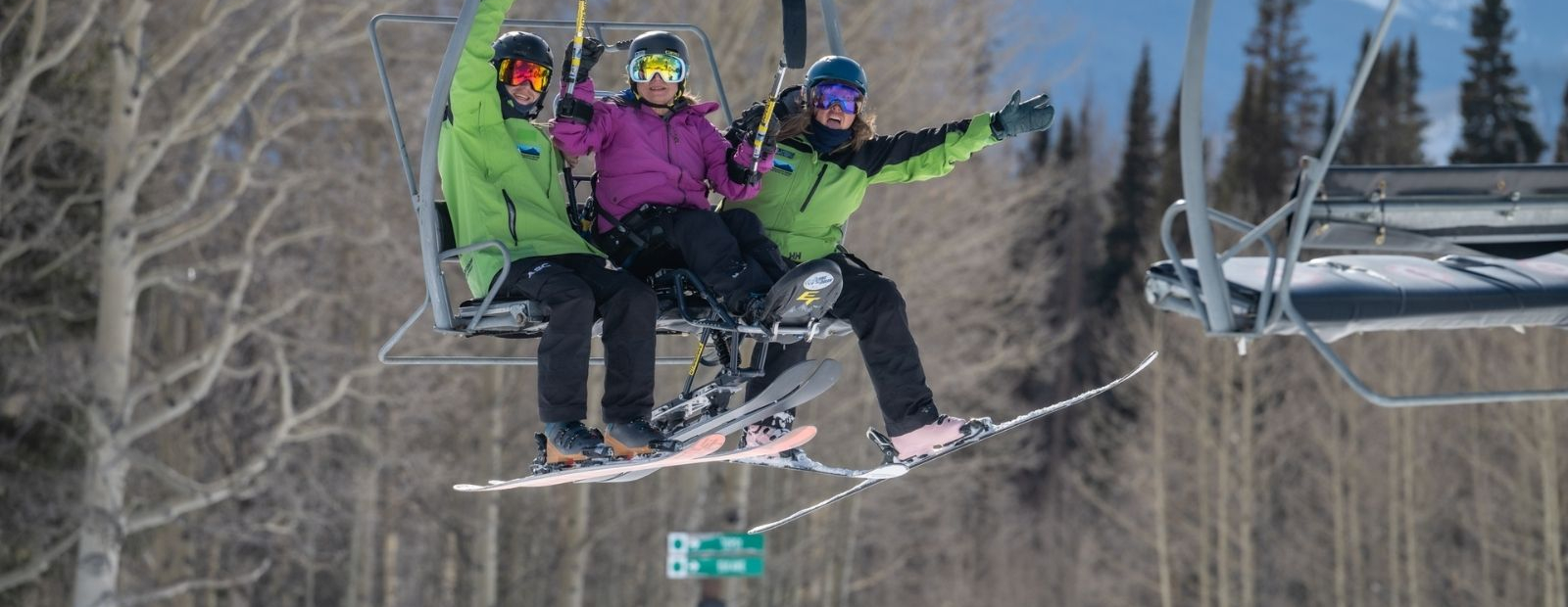 Skiers on a lift smiling and waving arms for photo.